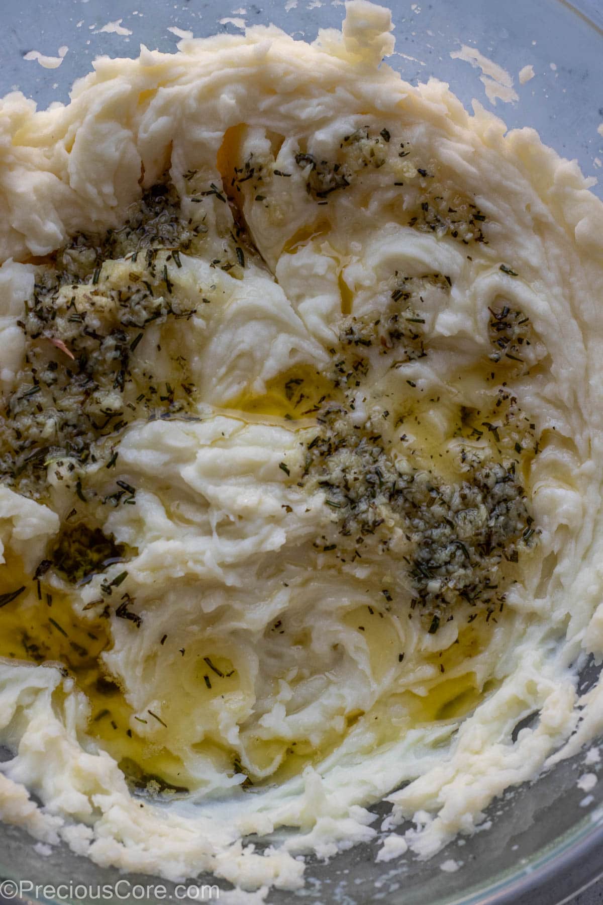 Melted butter and minced garlic and rosemary over mashed potatoes in a bowl.