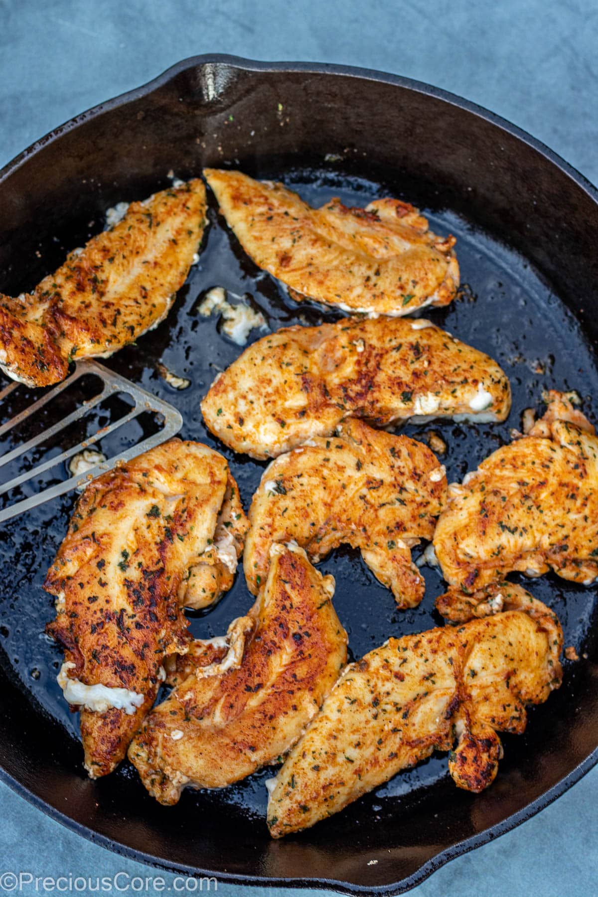 Chicken tenders in a pan with a fish spatula.