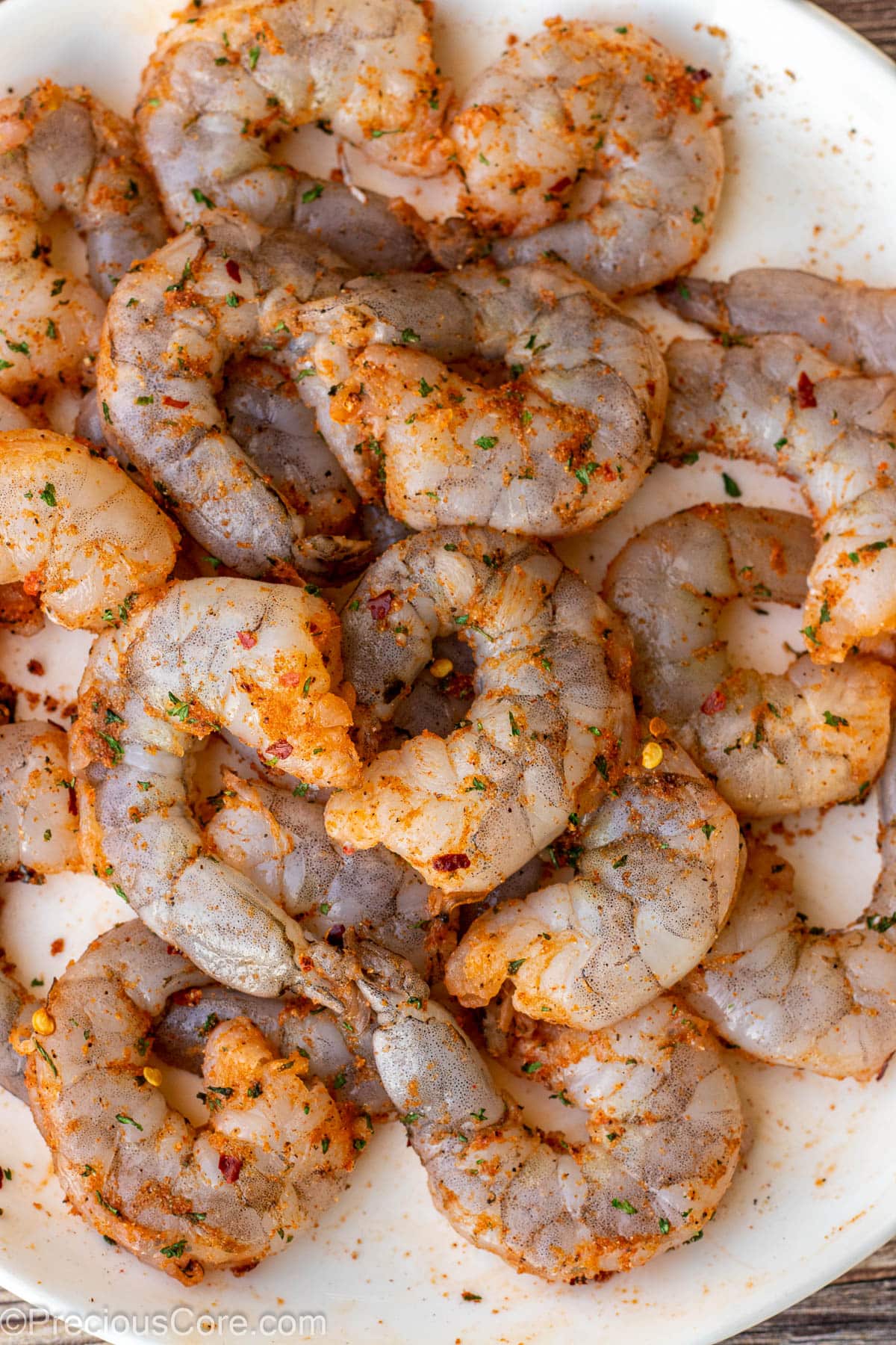 Raw seasoned shrimp on a white plate.