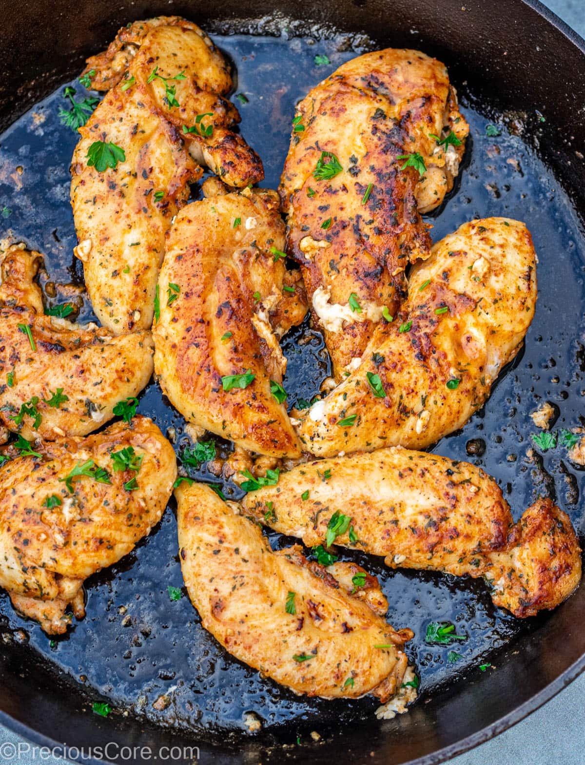 Chicken tenderloins cooking in a cast iron skillet.