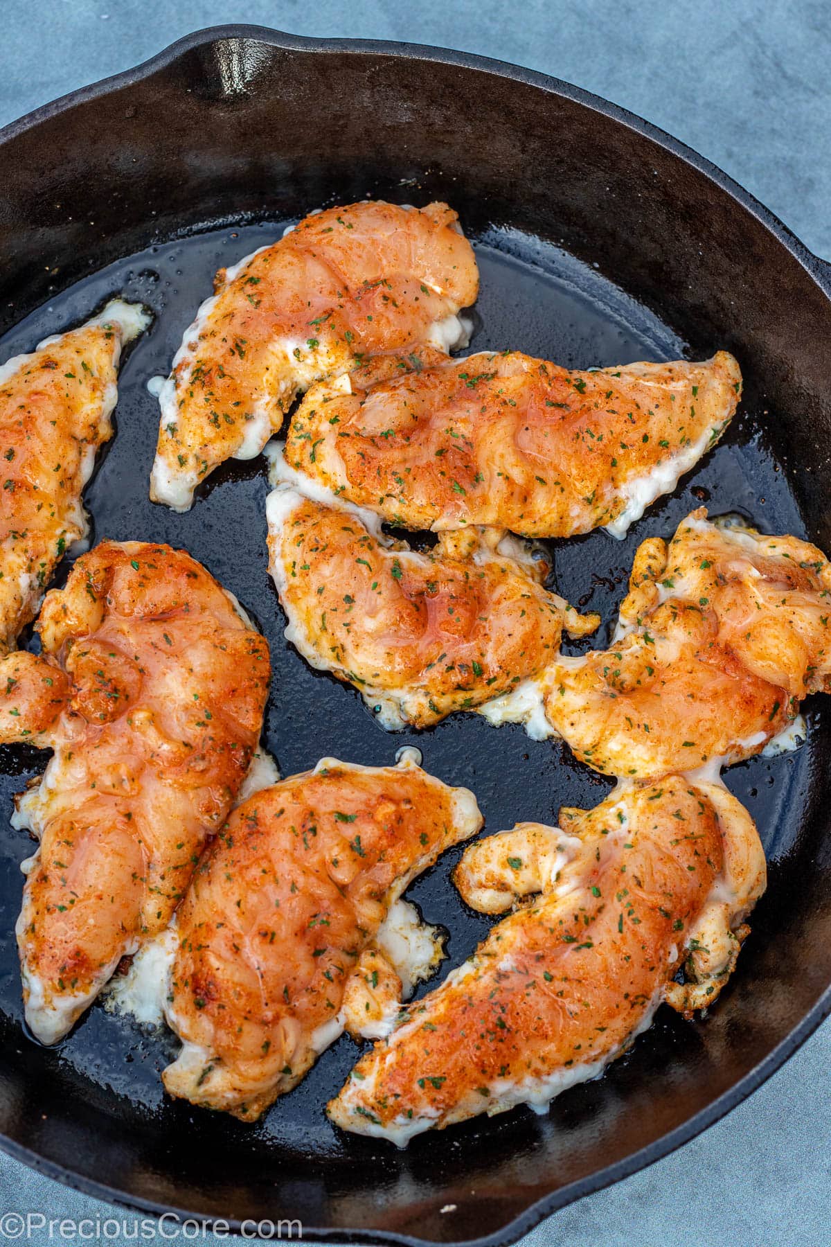 Raw chicken tenders searing in a skillet.
