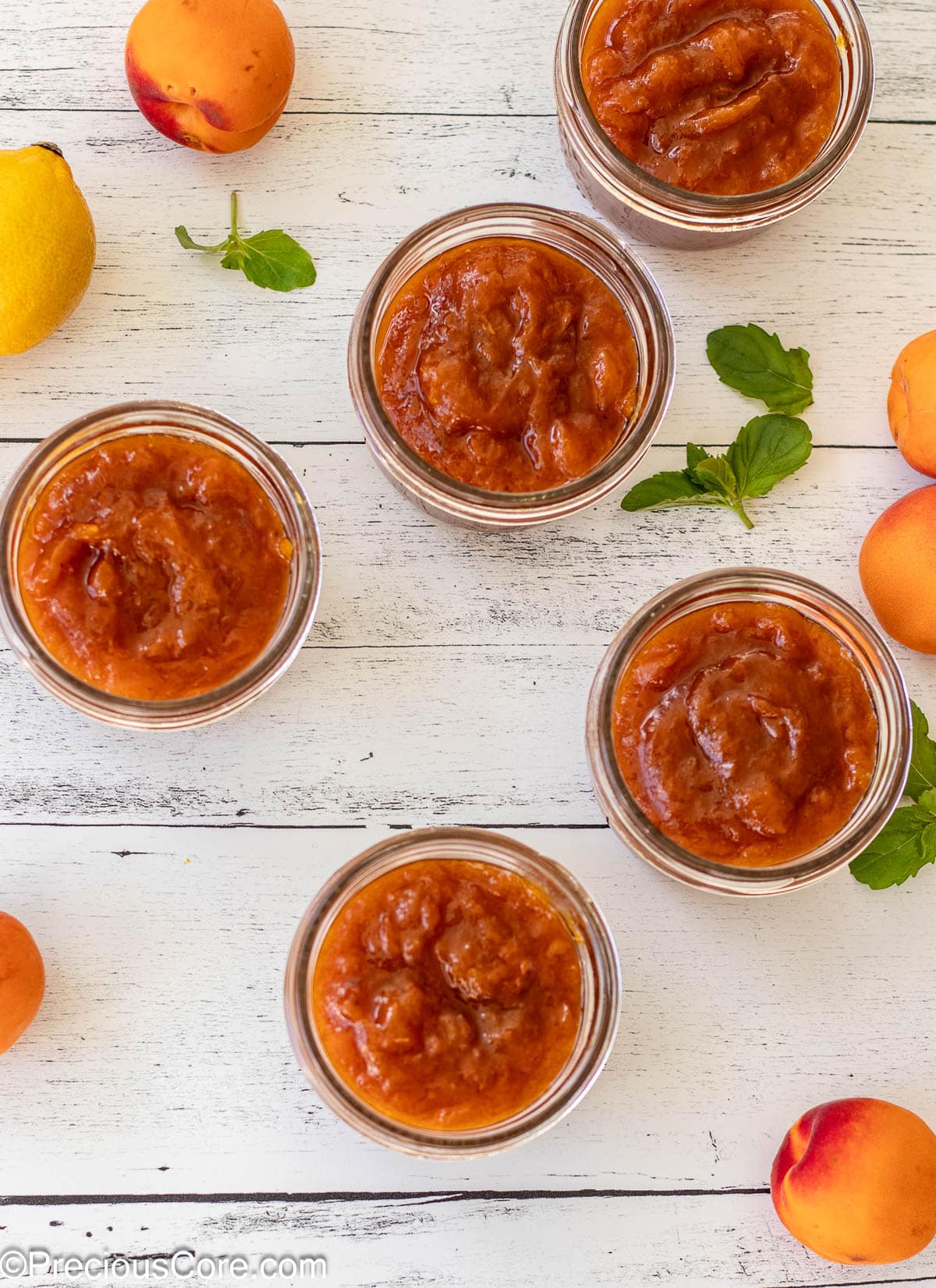 5 open jars filled with apricot preserves.
