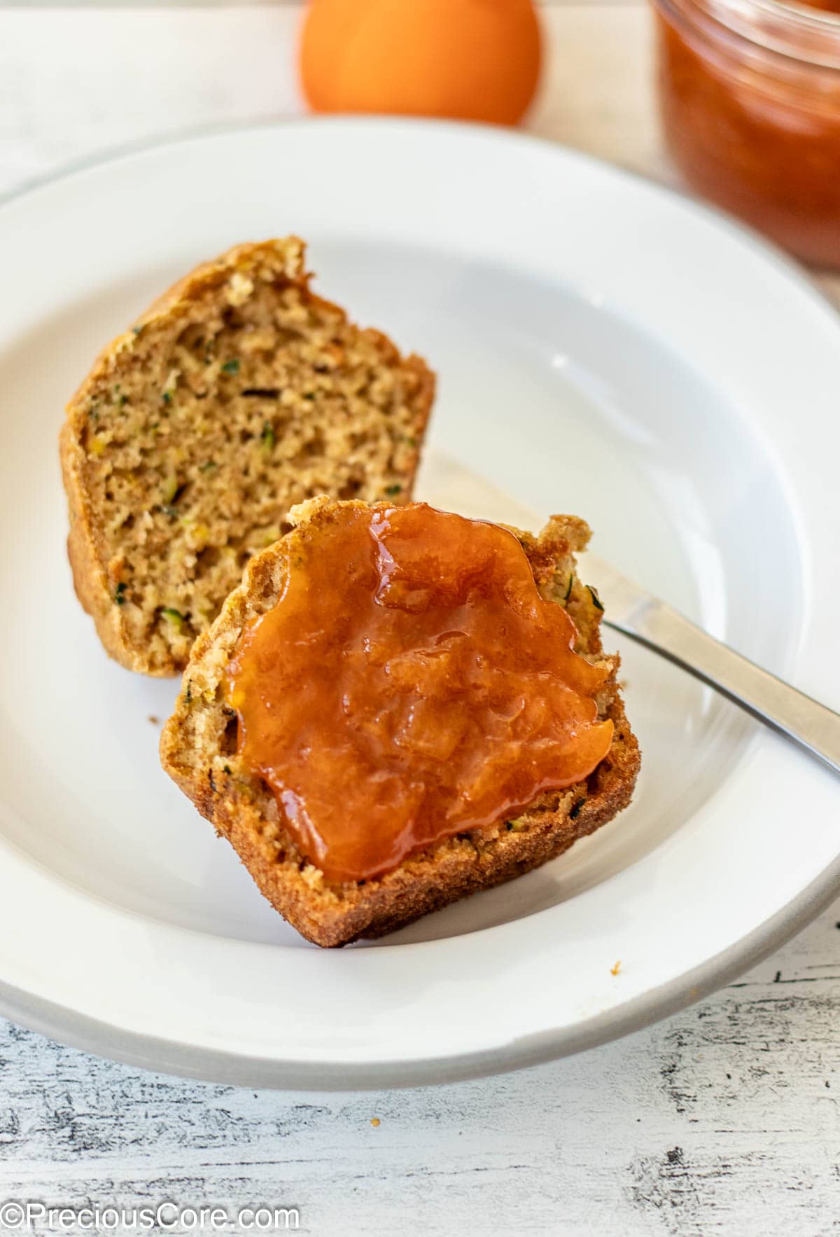 A zucchini muffin with apricot preserves spread on one half.