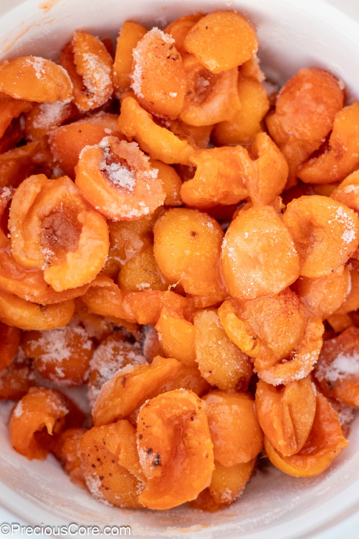 Halved apricots mixed with granulated sugar in a white bowl.