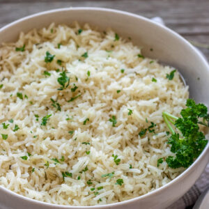 A bowl of garlic herb rice topped with minced fresh parsley.