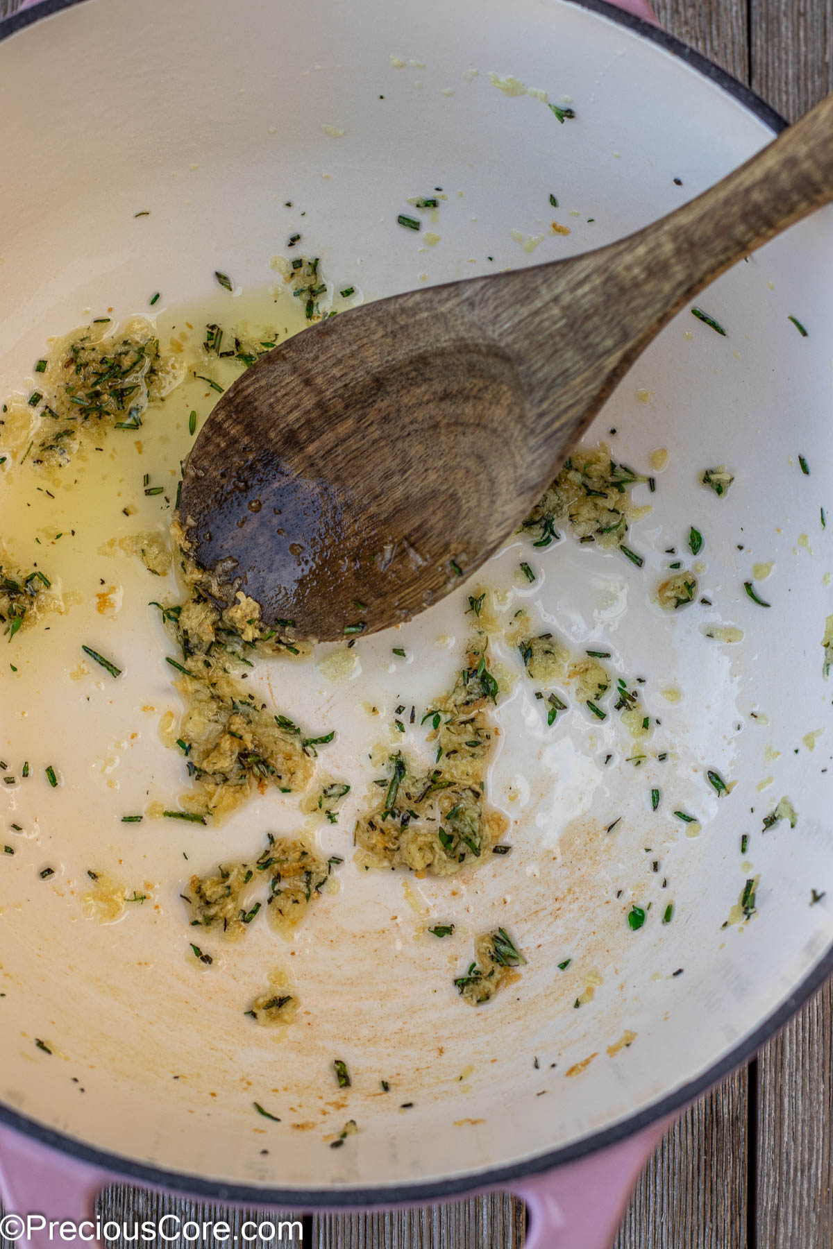 Garlic and fresh herbs sauteeing in olive oil in a cast iron enamel pot.