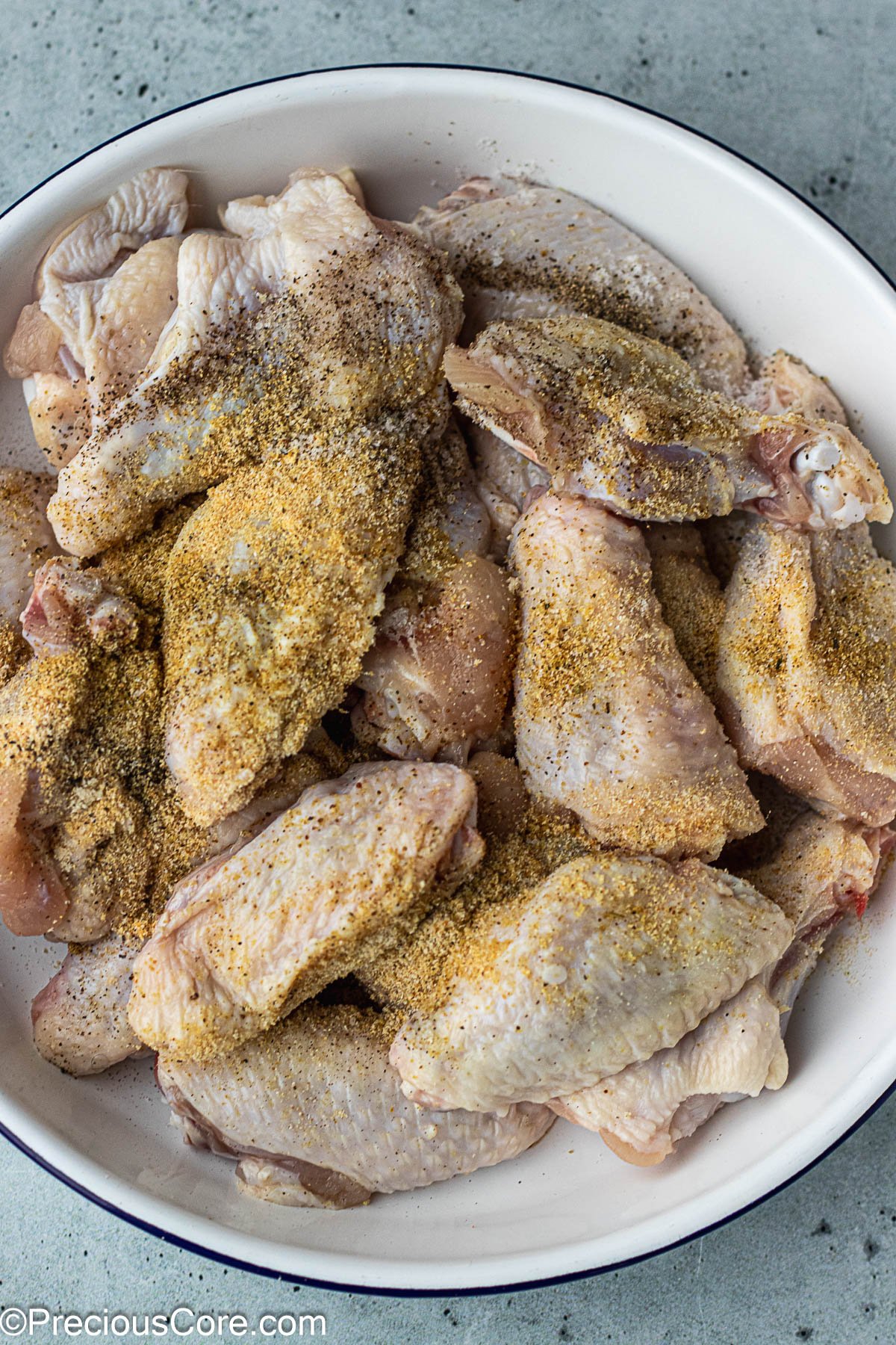 Chicken wings in a white bowl with powdered seasoning on top.