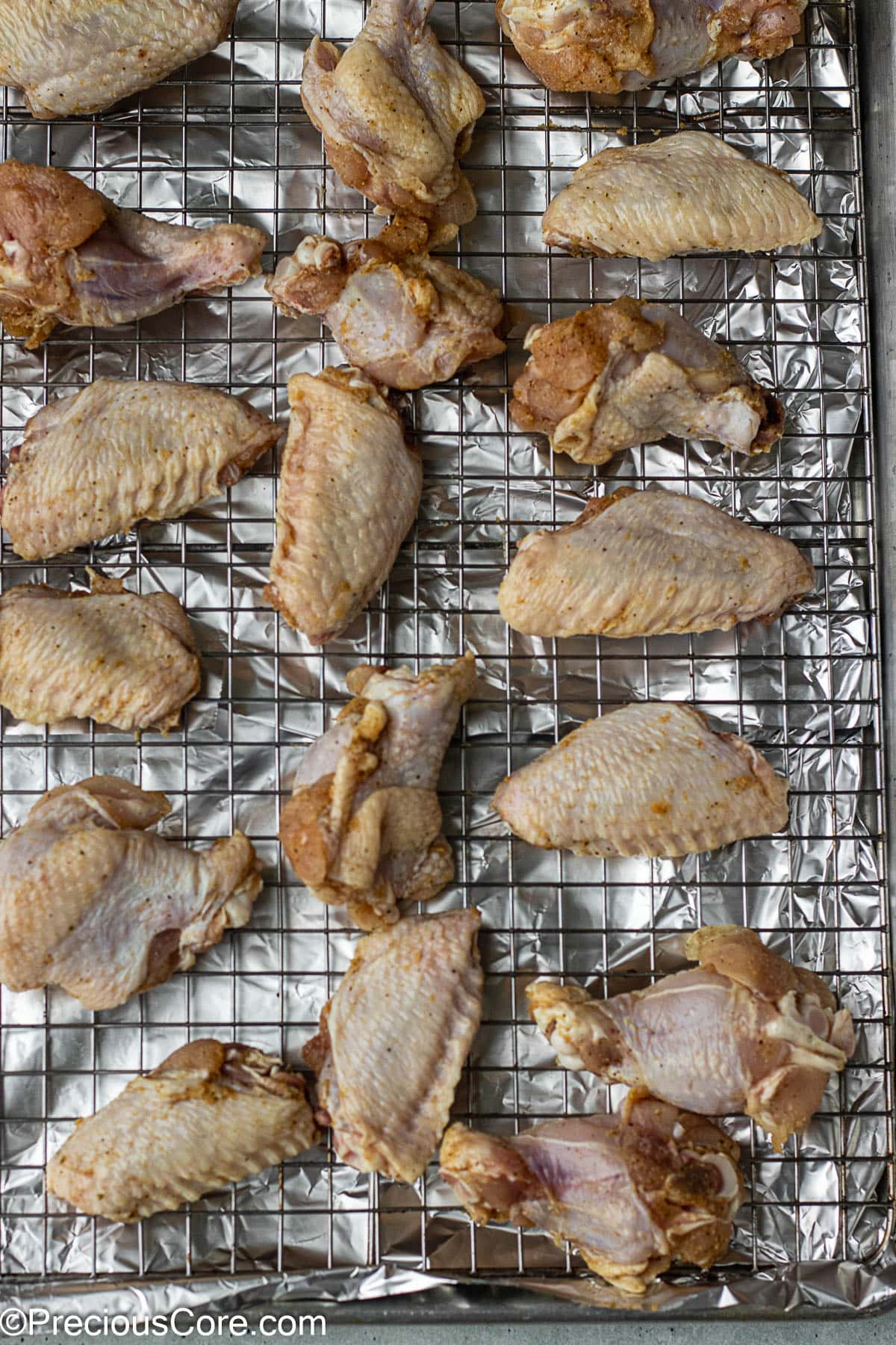 Raw chicken on a rack placed on a baking sheet.