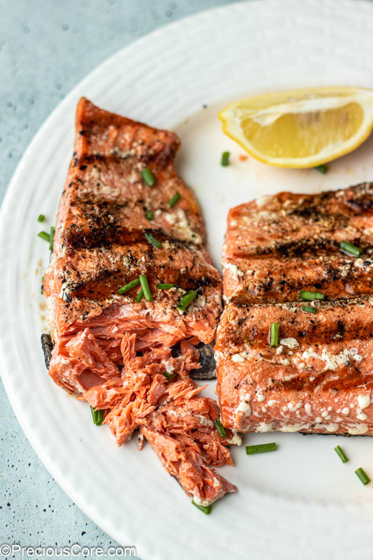 2 grilled salmon on a plate with one flaked with a fork.
