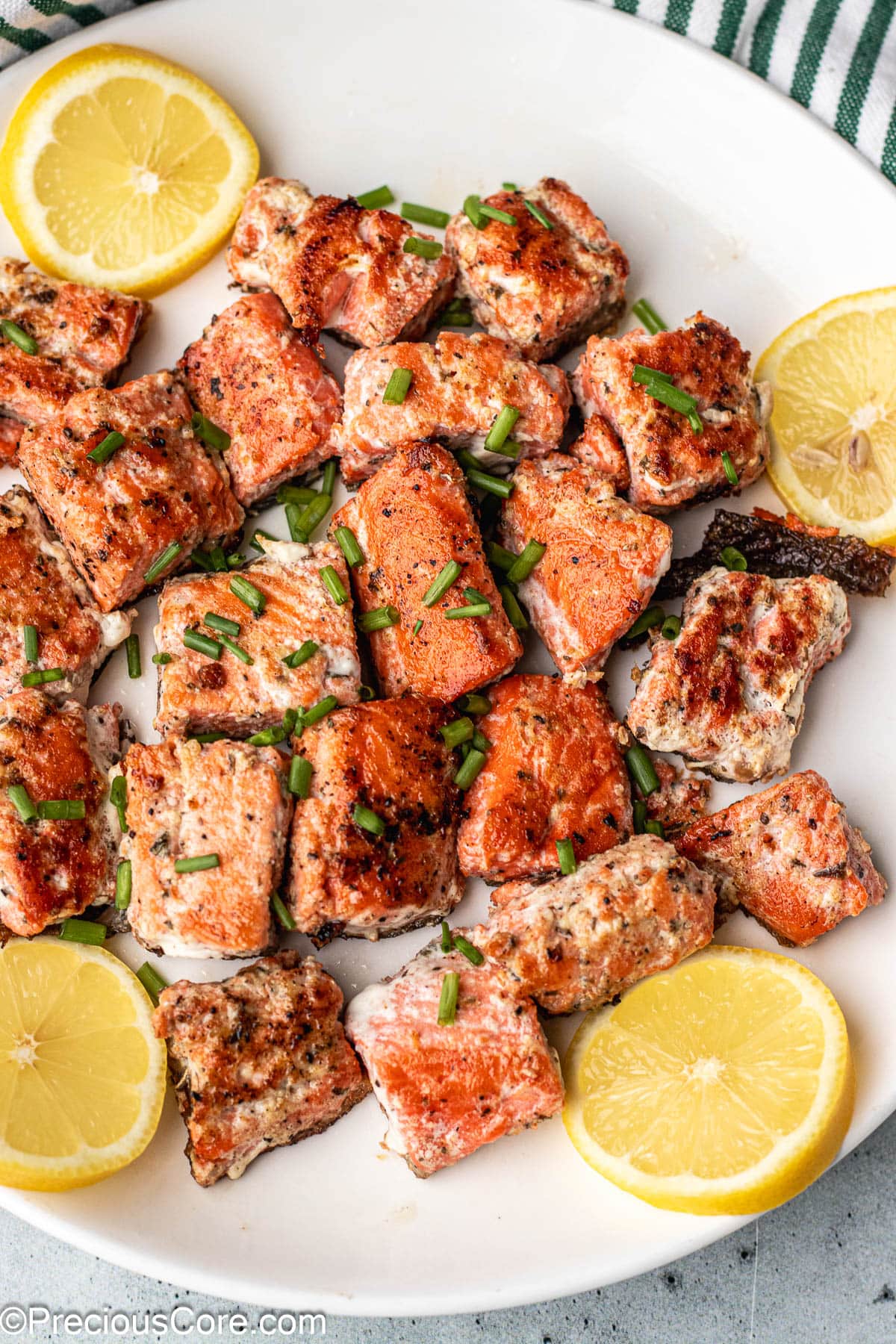 Bites of salmon on a white plate garnished with lemon slices.