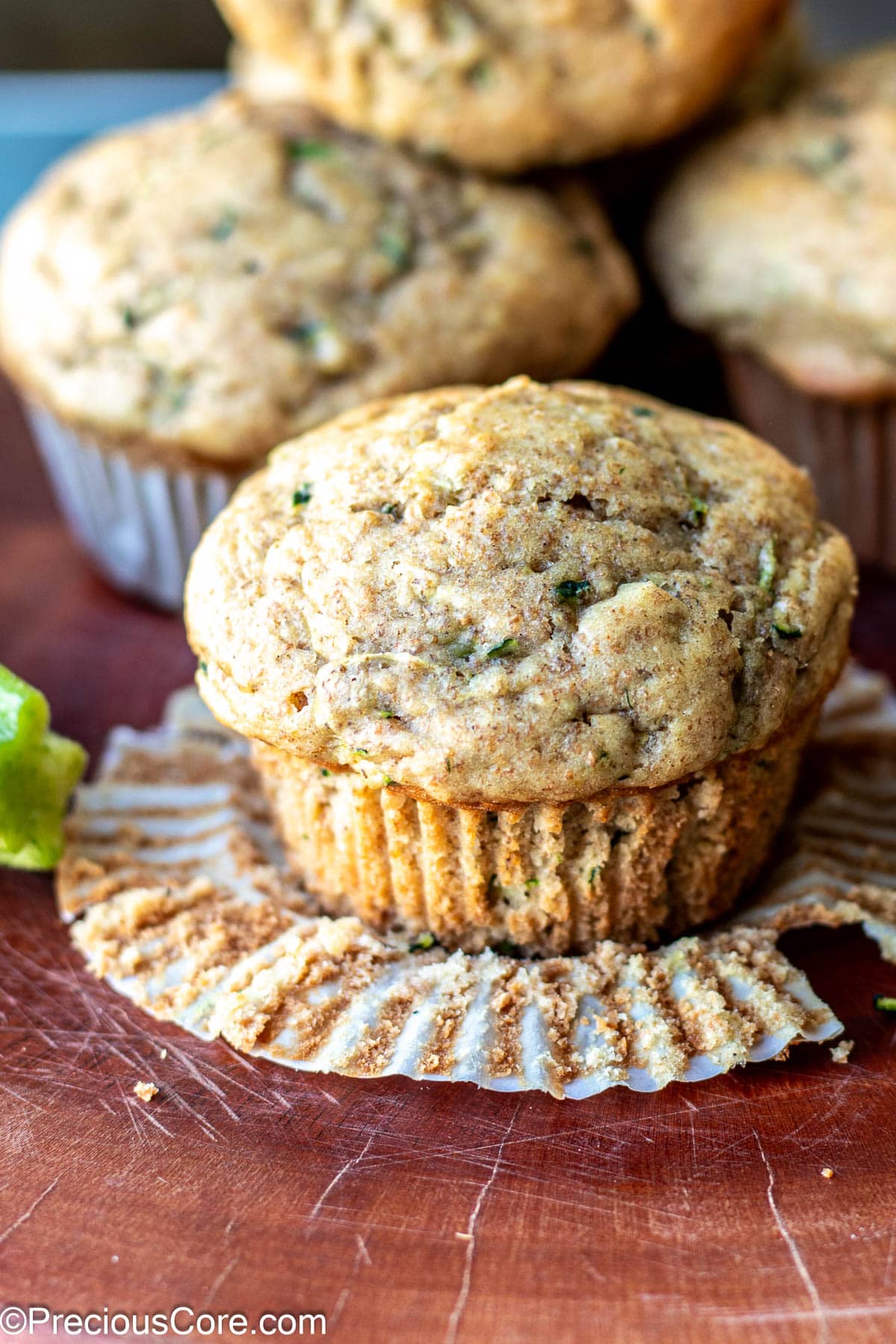 Zucchini muffin in foreground with paper lining peeled from it.