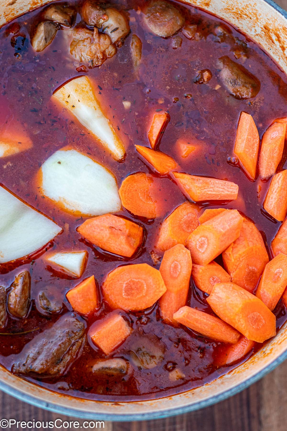 Raw carrots and potatoes added to pot of stew.