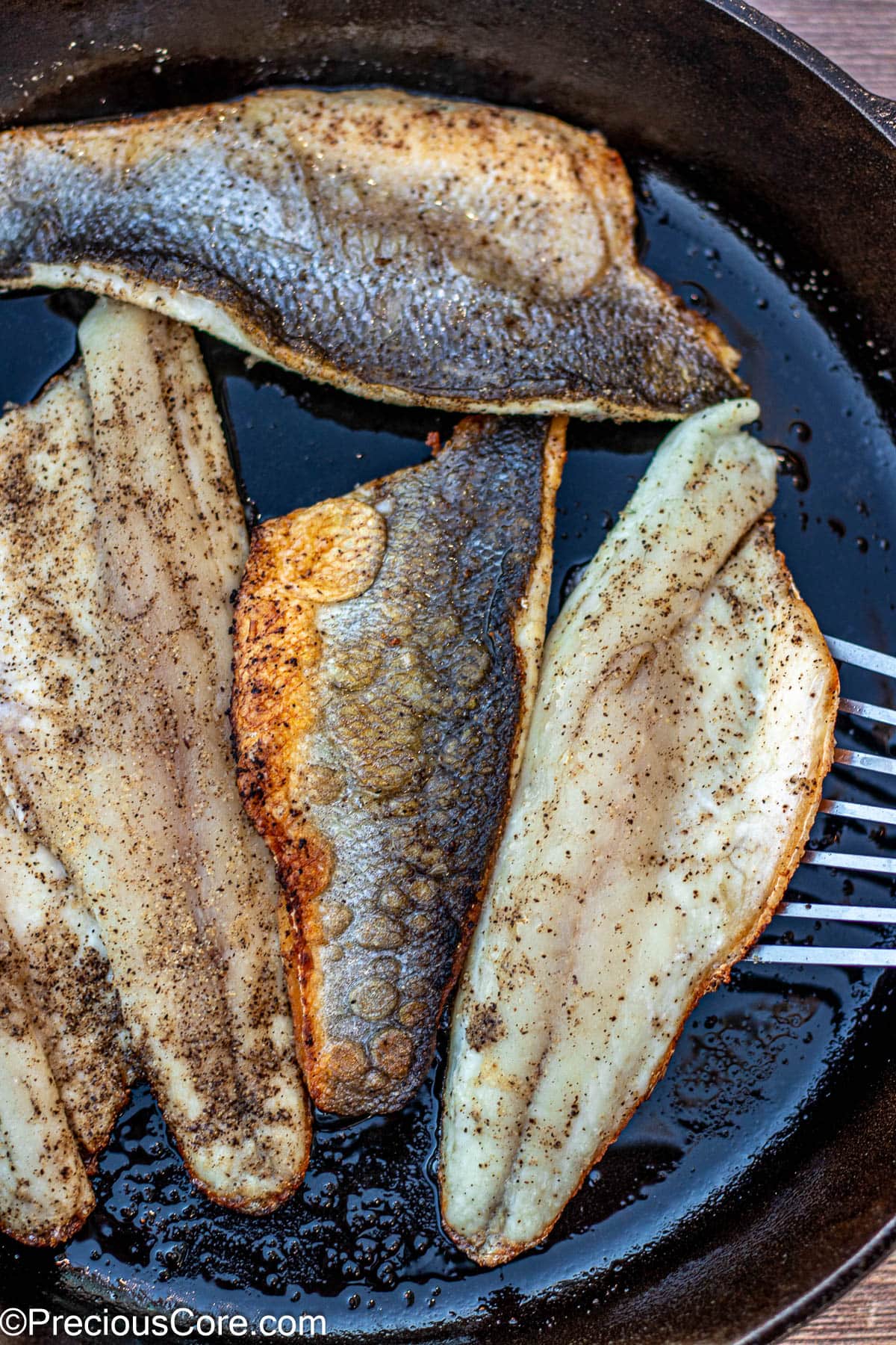 Fish spatula flipping cooked sea bass.