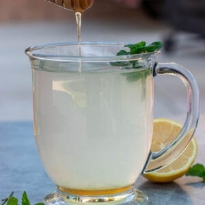 Honey dipper dripping honey into a cup of honey lemon tea.