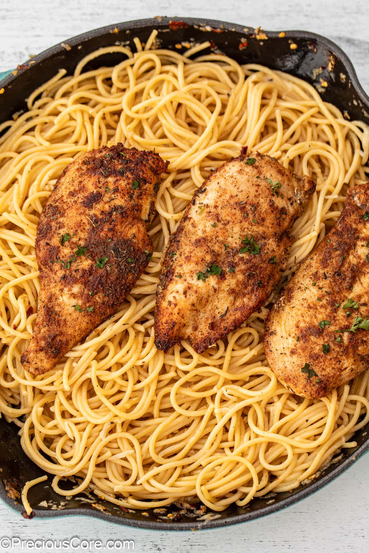 A skillet of garlic butter spaghetti topped with chicken.