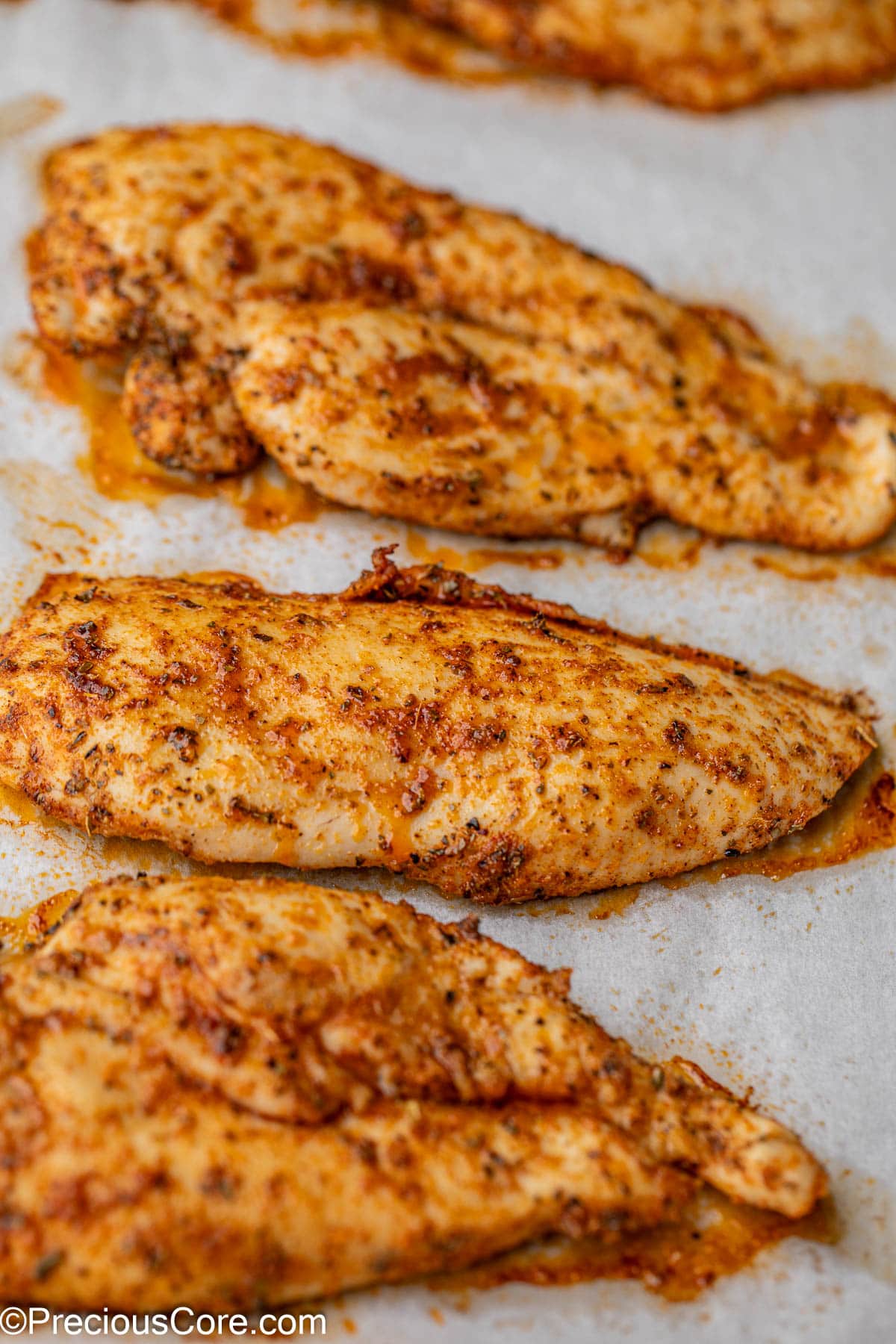 Baked thin sliced chicken breasts on parchment paper-lined baking sheet.