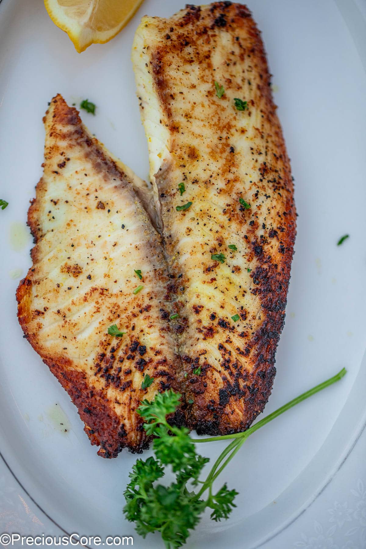 A cooked fish fillet garnished with minced parsley.