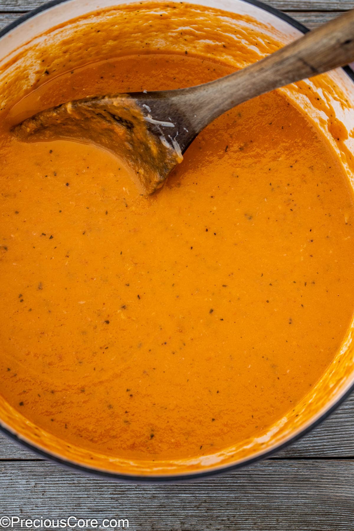 Tomato soup in a pot with a wooden spoon in the pot.