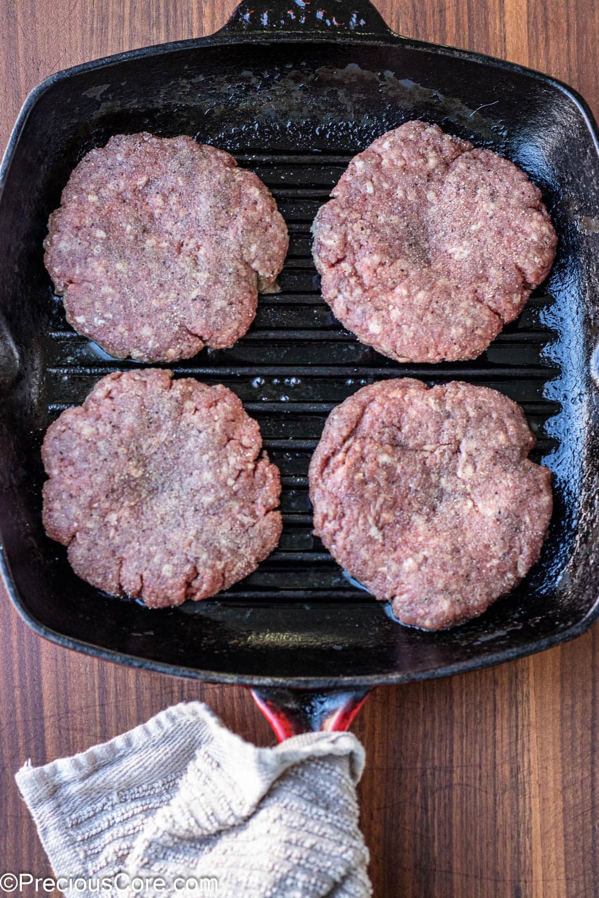 Seasoned burger patties in a square grill pan.
