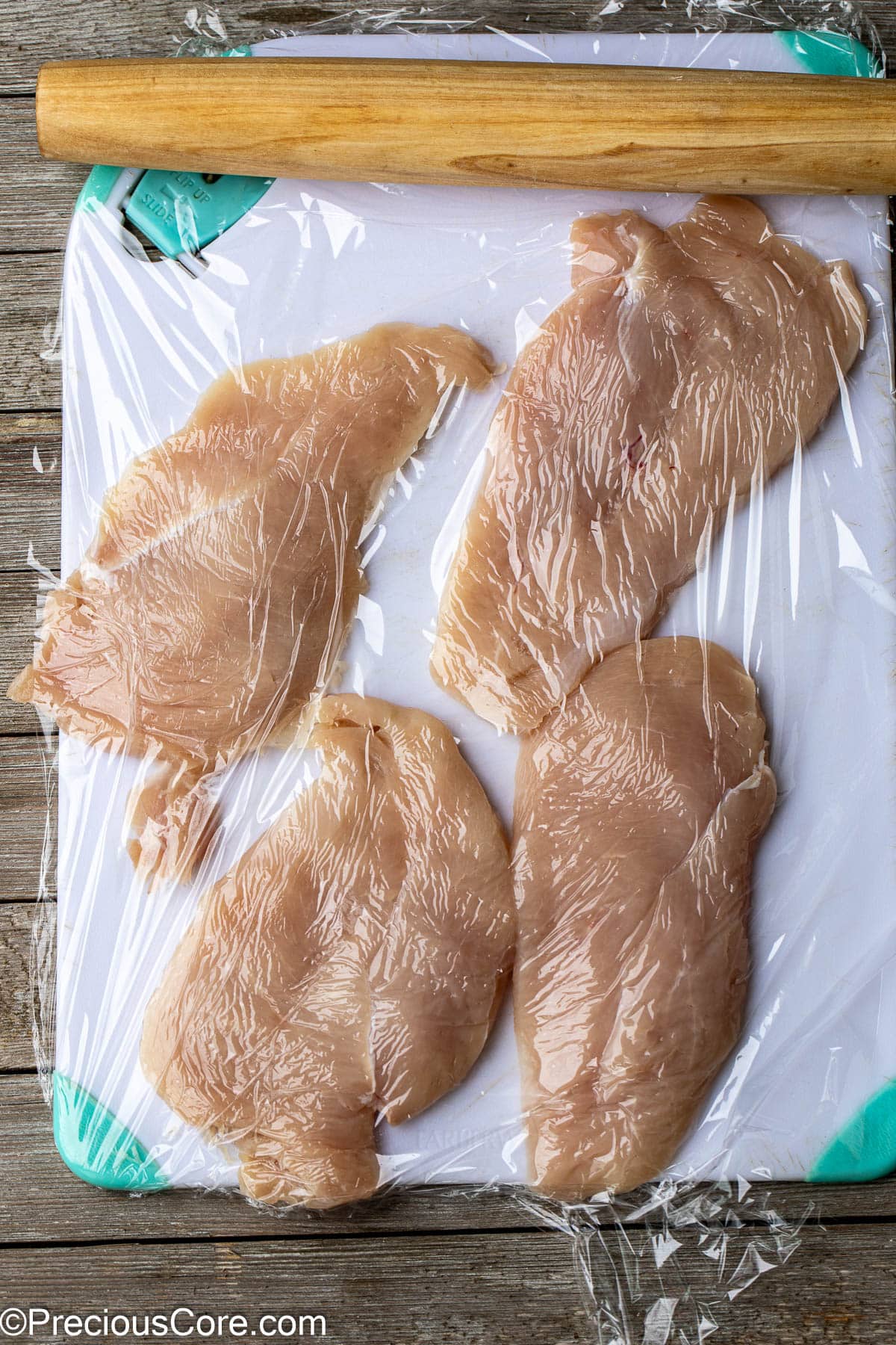 Chicken breasts flatted with rolling pin on chopping board.