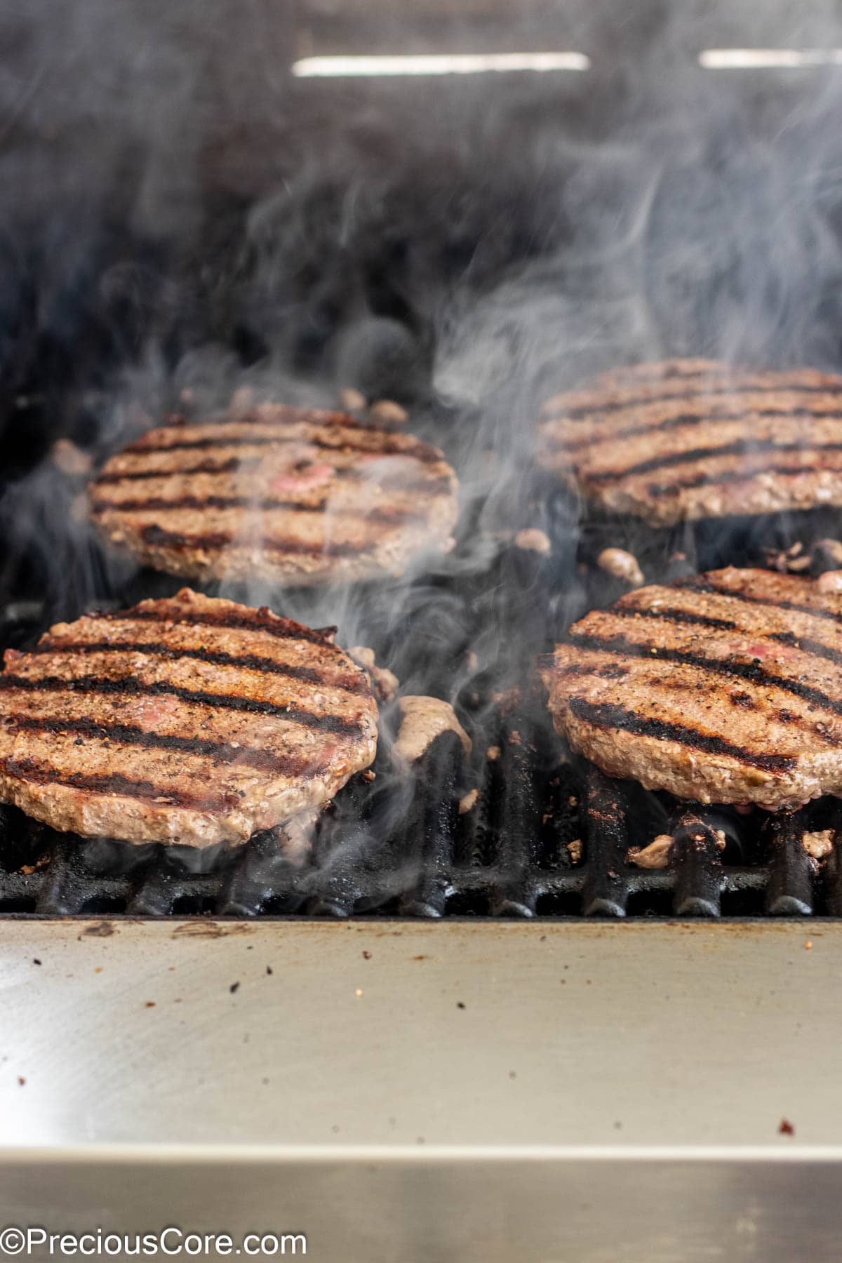 Burgers with grill marks being grilled on the outside grill.
