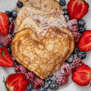Heart shaped pancakes on a plate with berries.