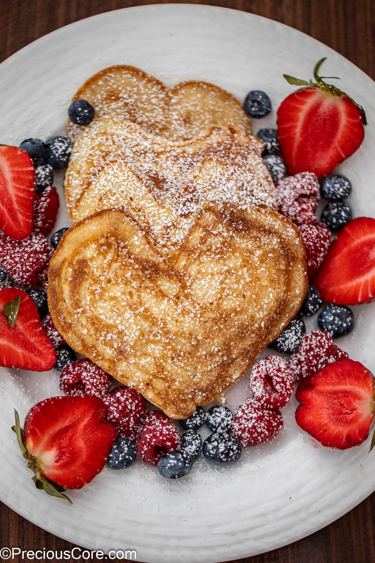 Heart shaped pancakes on a plate with berries.