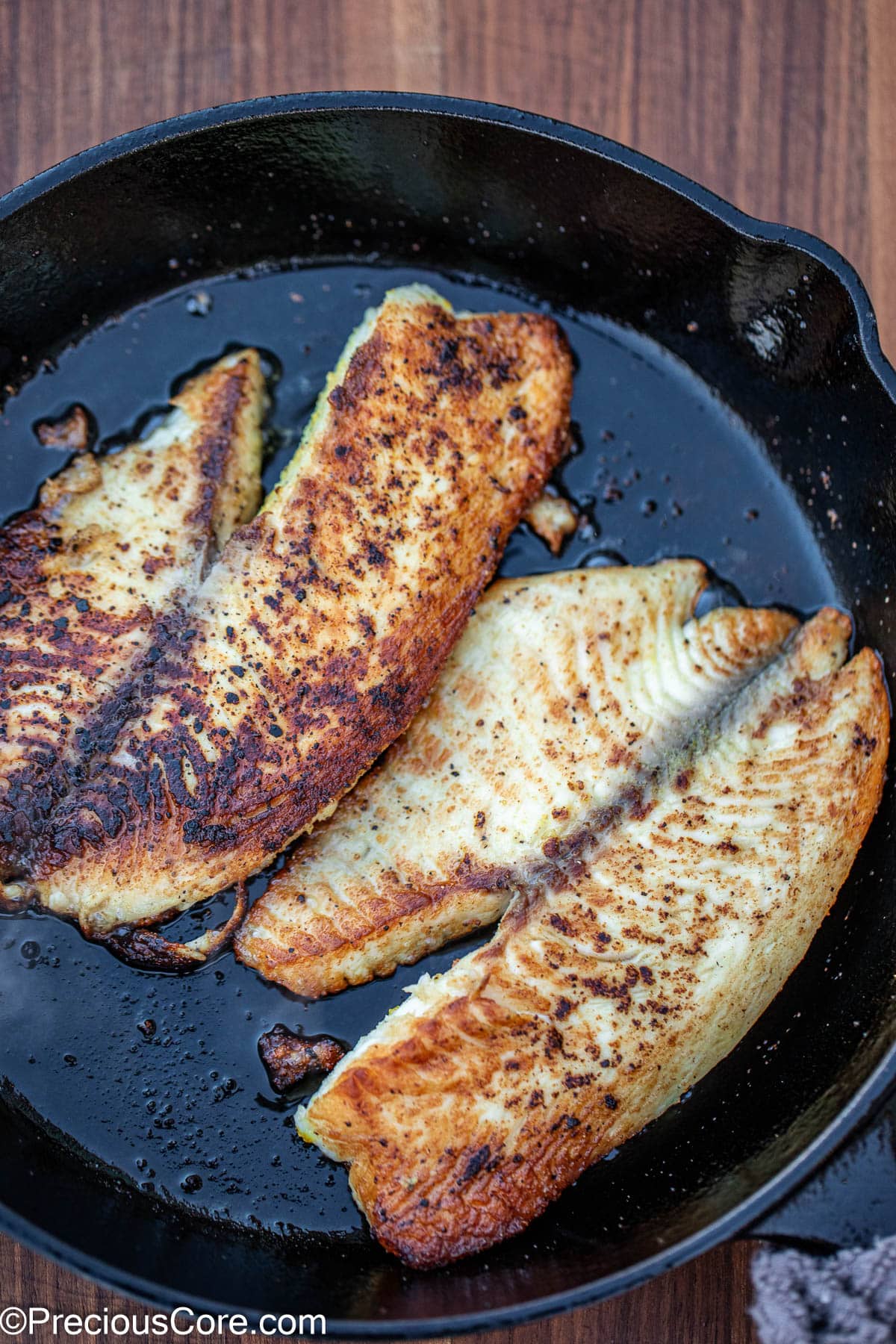 2 cooked fish fillets in a cast iron skillet.