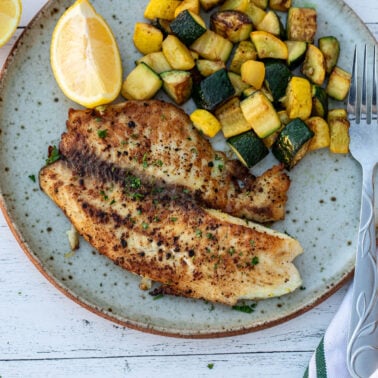 Square image of tilapia and zucchini on a plate.