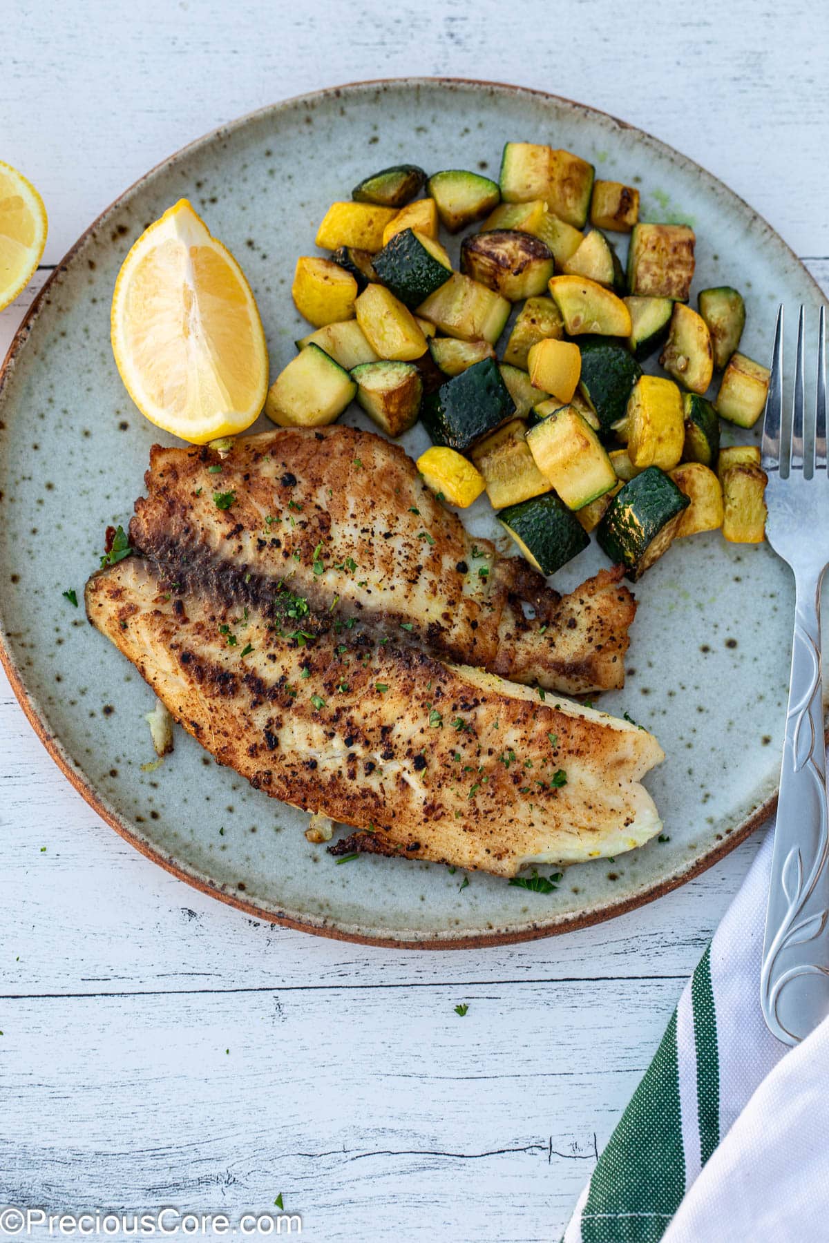 Lemon pepper tilapia on a plate with sautéed zucchini.