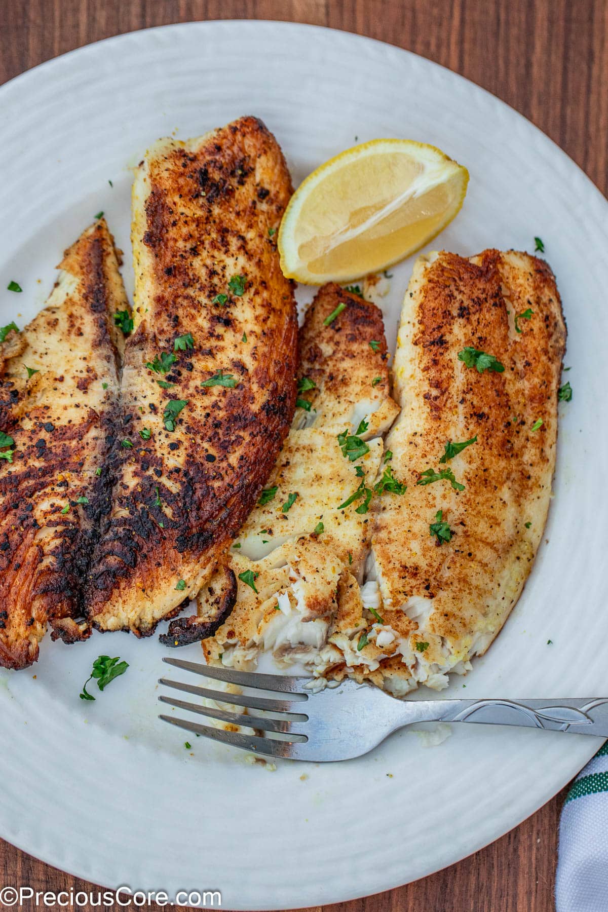 2 lemon pepper tilapia fillets on a white plate.