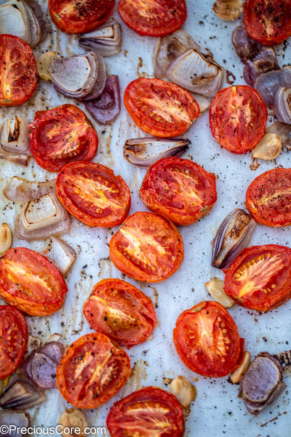 Roasted tomatoes onions and garlic on a sheet pan.