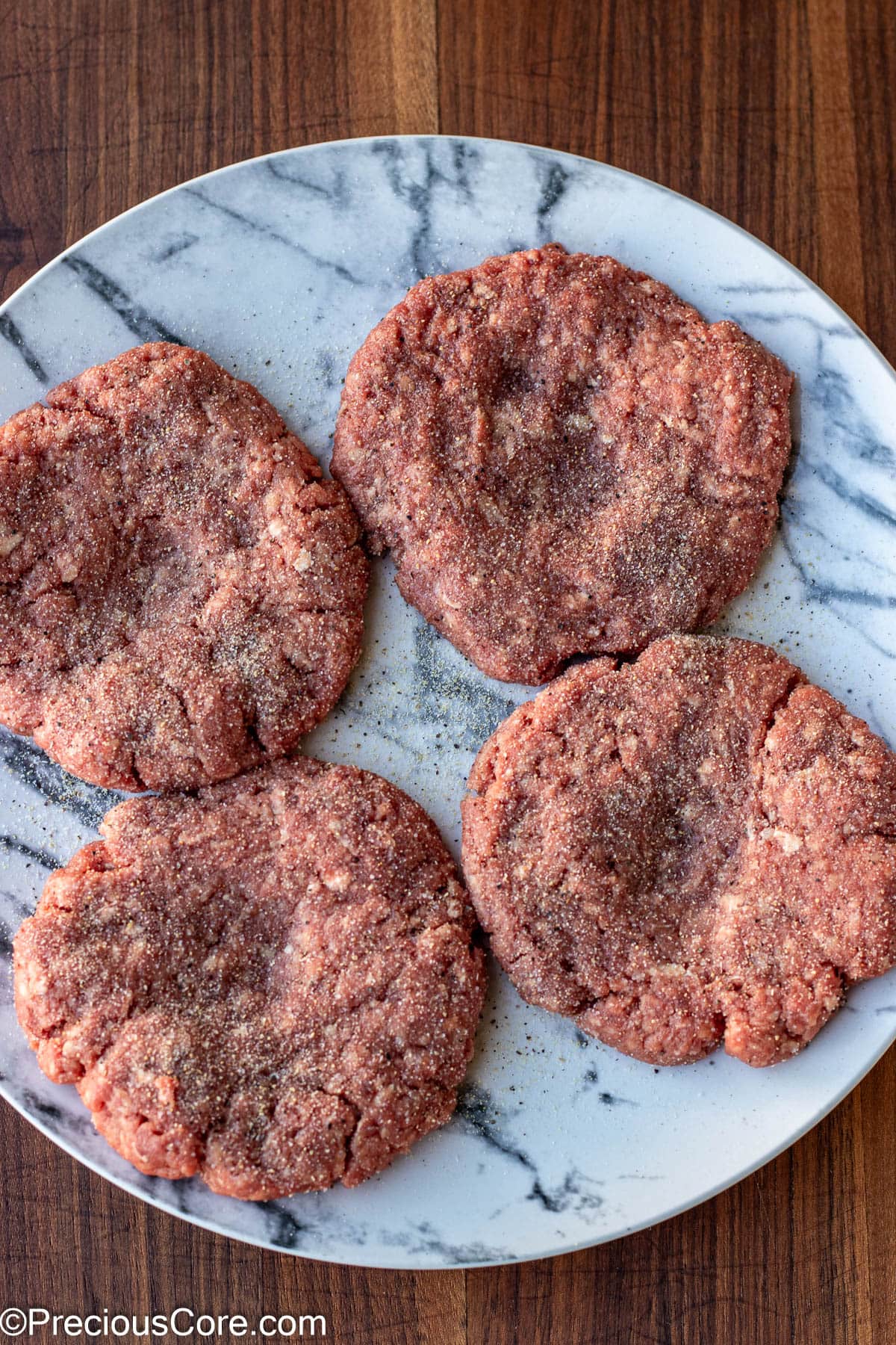 Seasoned burger patties on a plate.