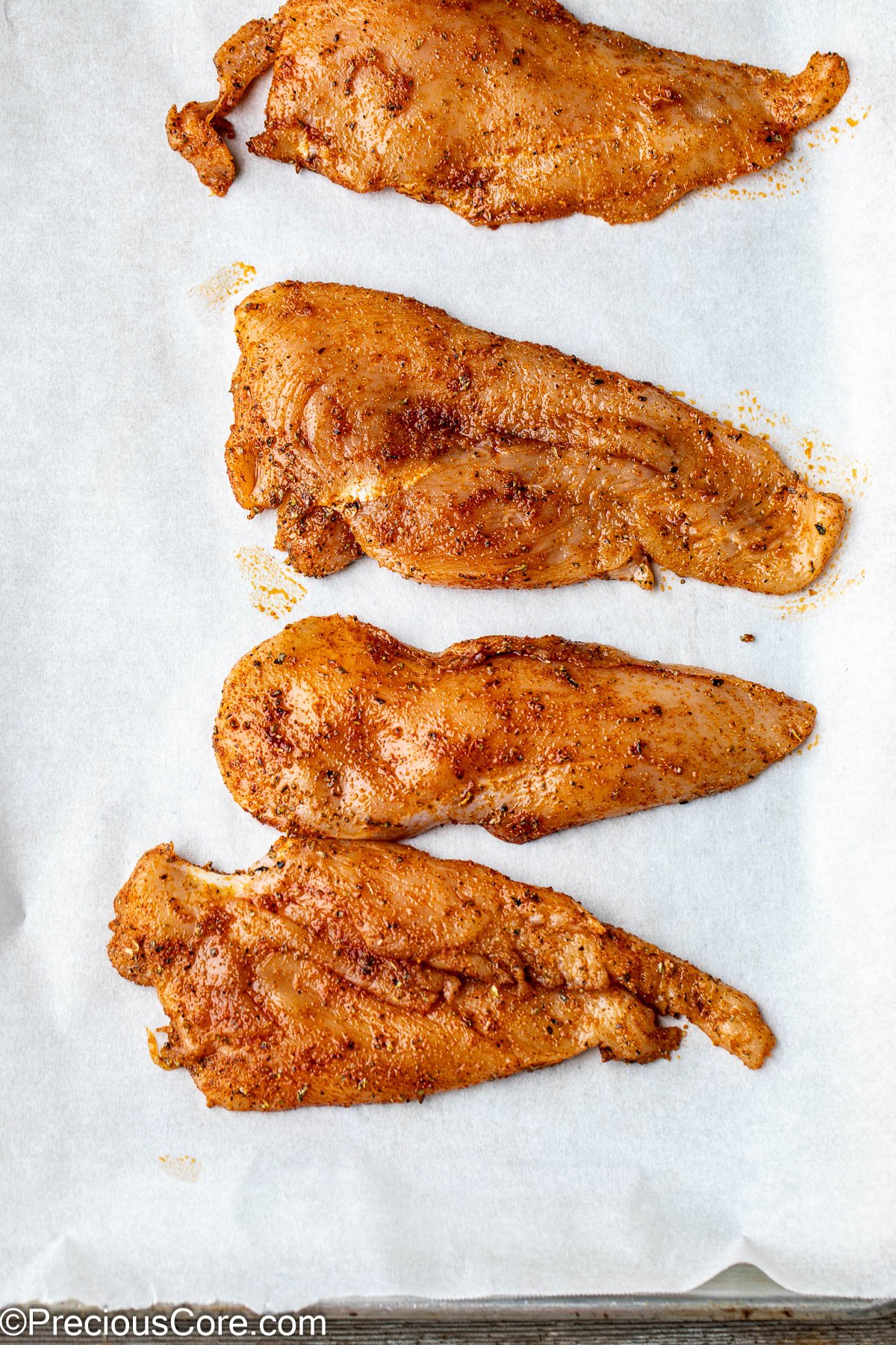 Seasoned thinly sliced chicken breasts on parchment paper.