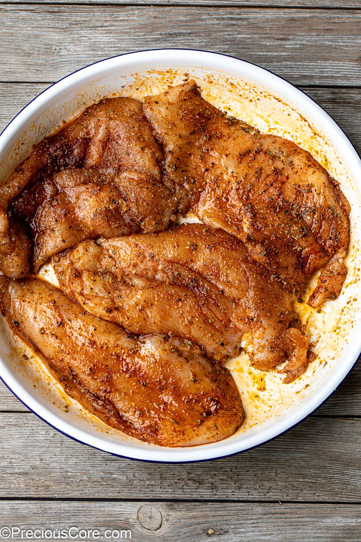 Seasoned thin chicken breasts in a white bowl.