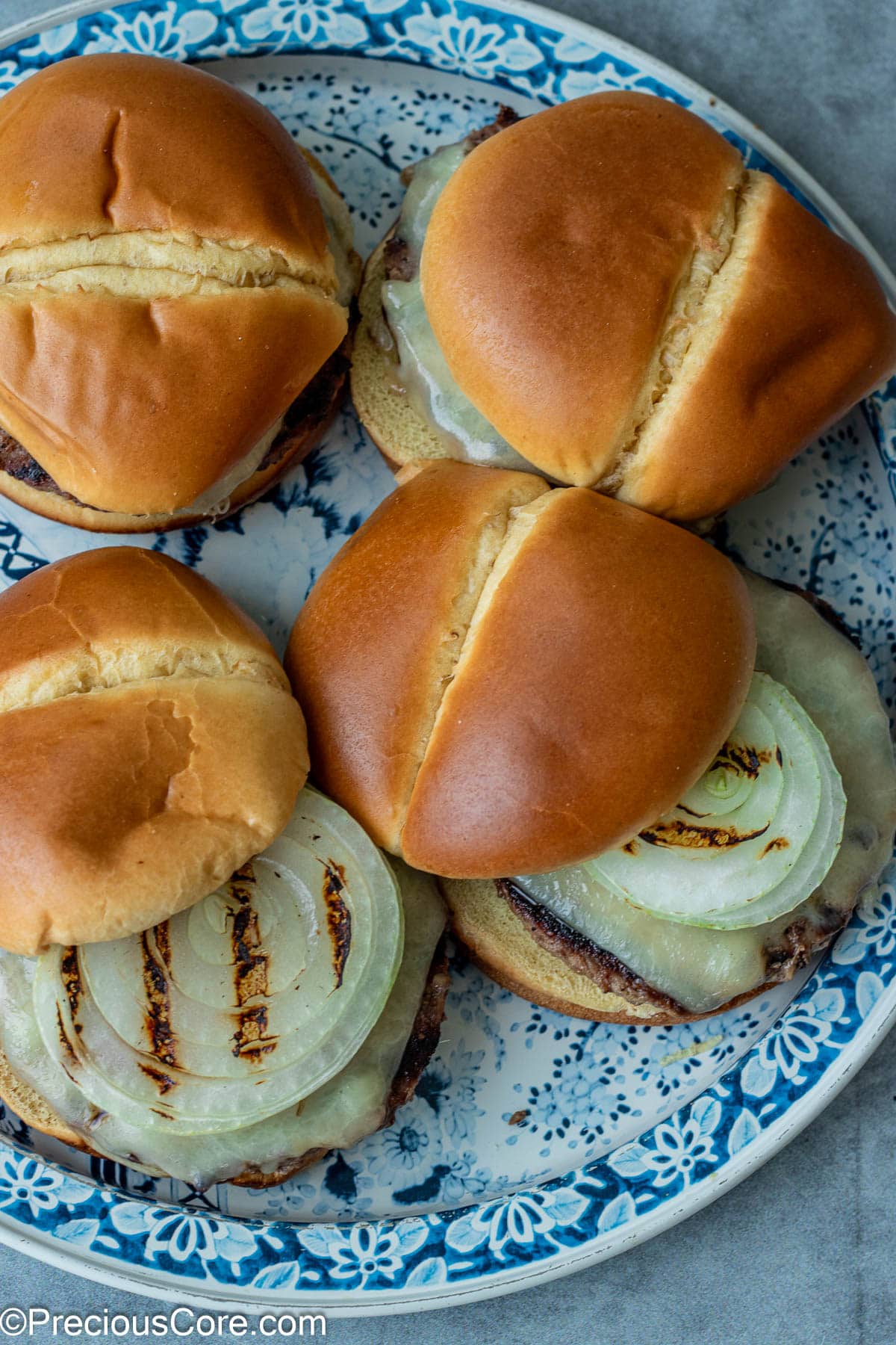 4 burgers with grilled onions on a round platter.
