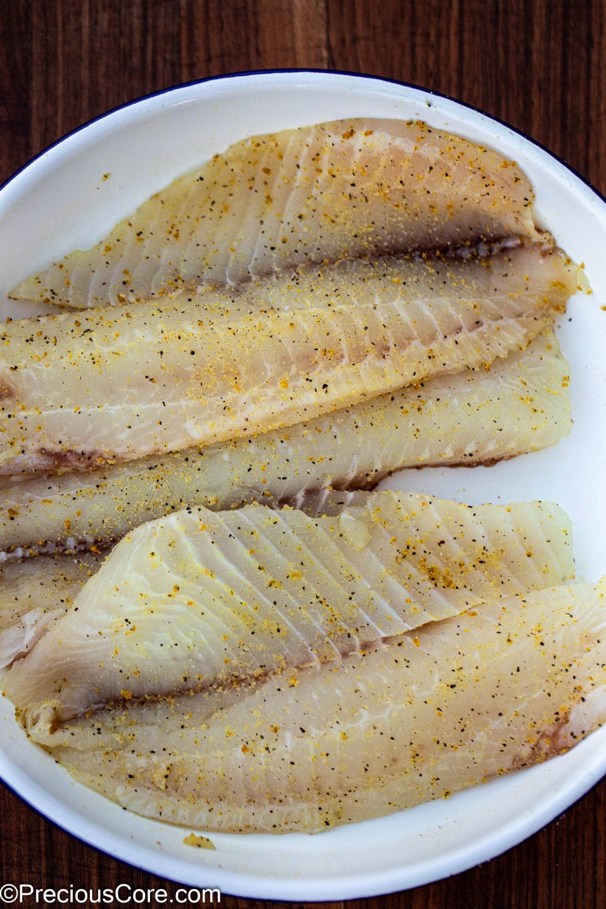 Seasoned tilapia fillets in a white bowl.