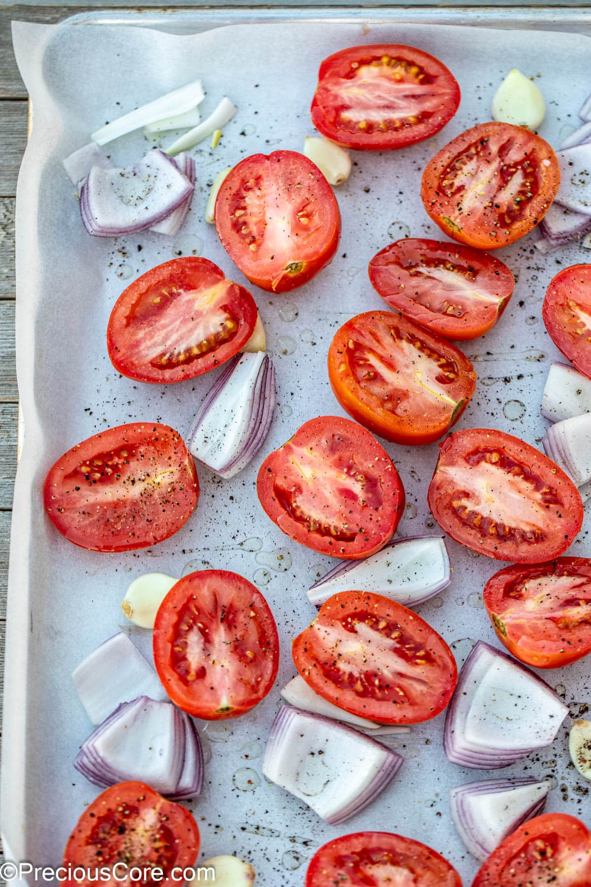 Halved Roma tomatoes, onions, and garlic on a sheet pan.