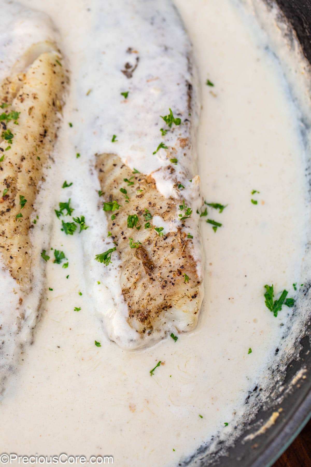 Fish in white sauce garnished with minced parsley.