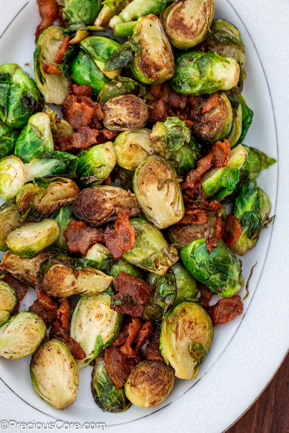 Cooked bacon and Brussels sprouts on a white serving plate.