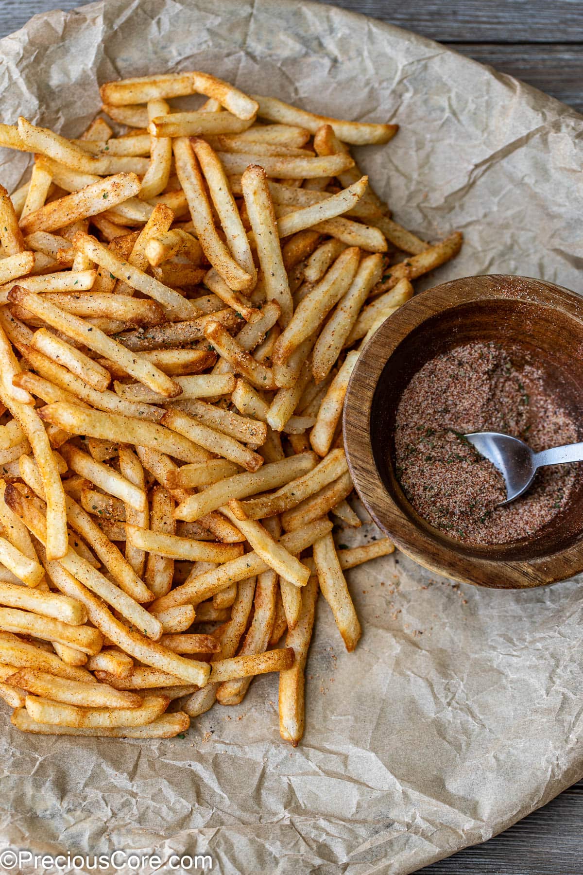 Fries on brown parchment paper with seasoning sprinkled on them.