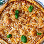 A cheese pizza on a round pizza tray, garnished with basil leaves.