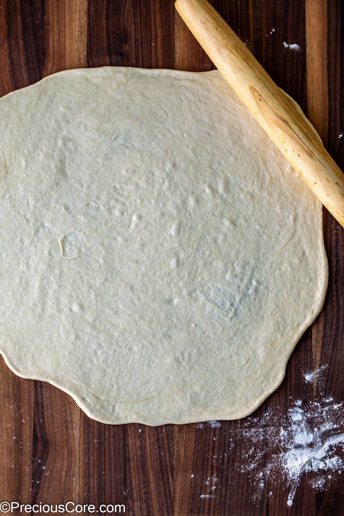 Pizza dough rolled out on chopping board.