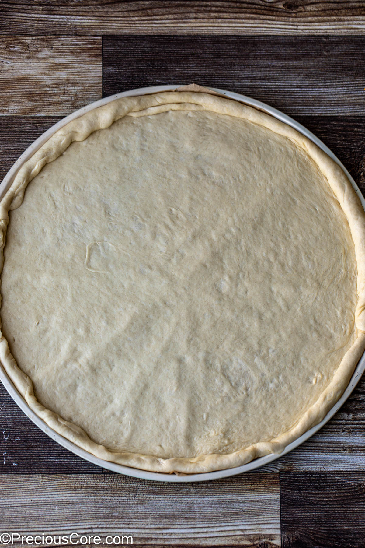 Pizza dough on pizza pan with edges tucked in.