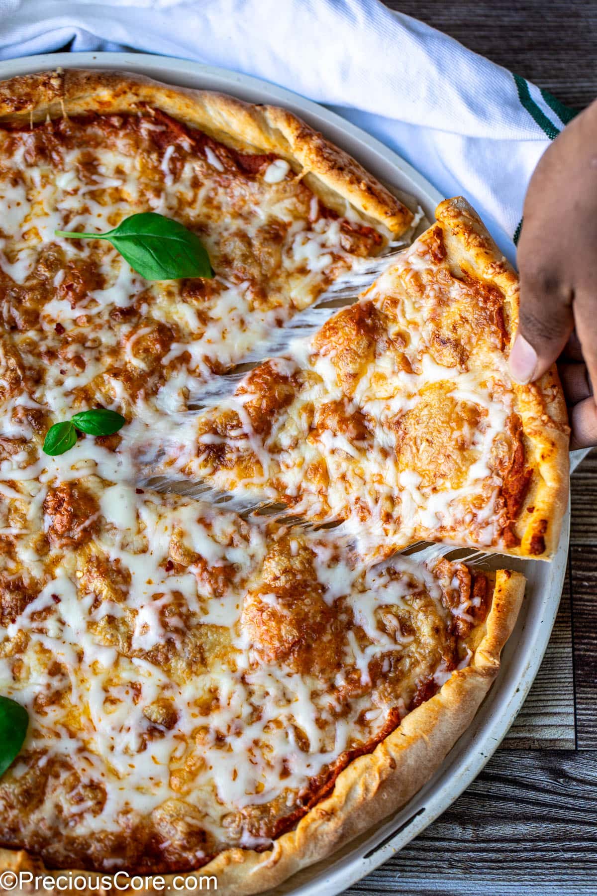 Hand pulling a slice of pizza with gooey cheese.