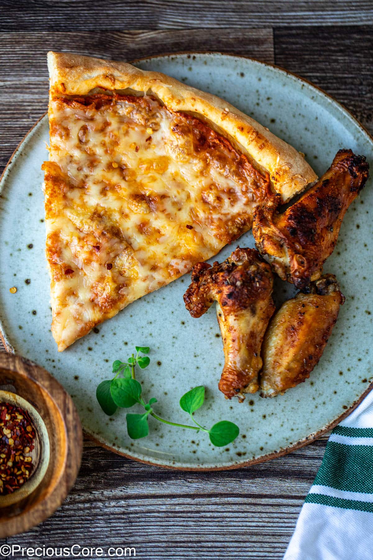 A slice of pizza on a plate with some chicken wings on the side.