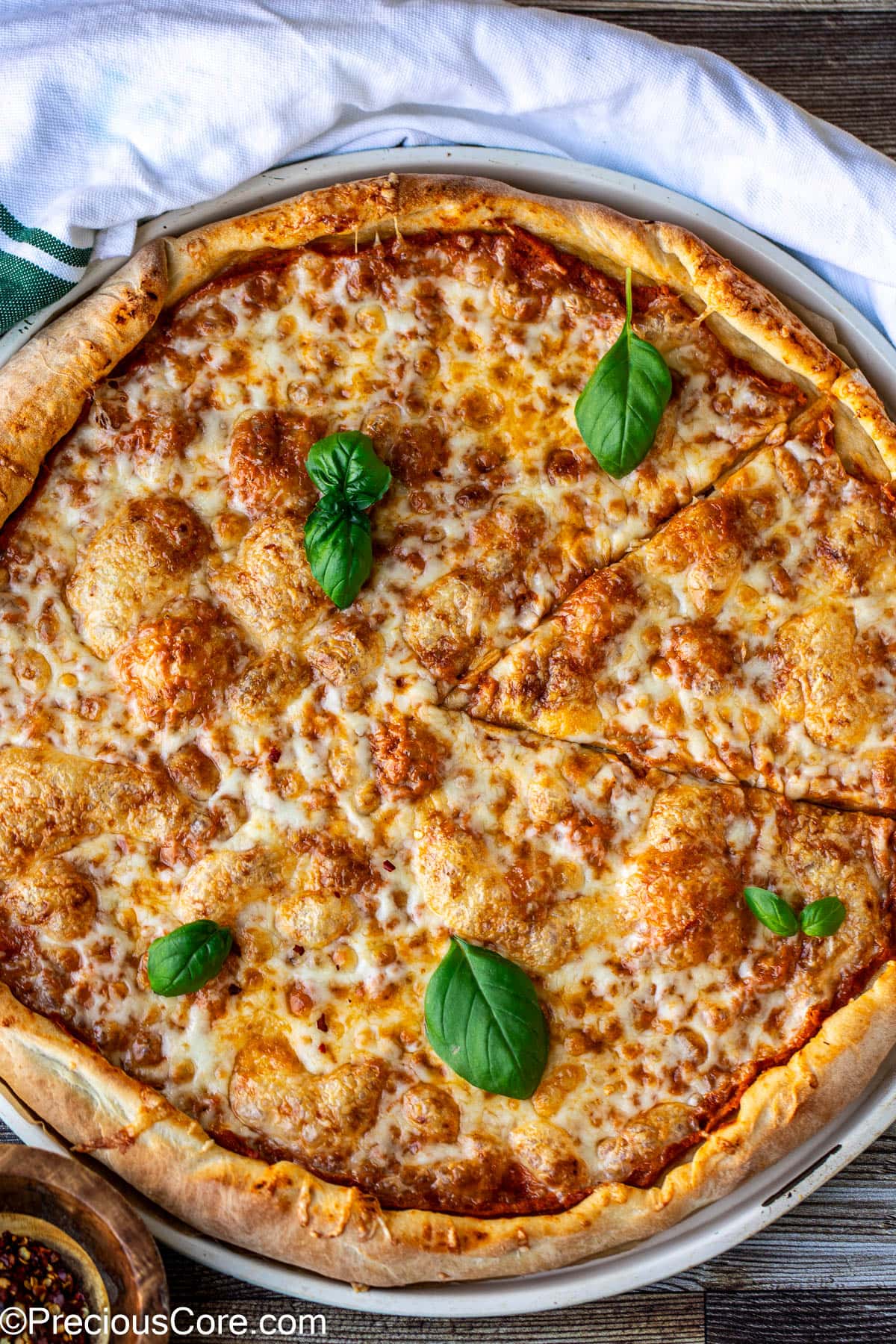 A cheese pizza on a round pizza tray, garnished with basil leaves.