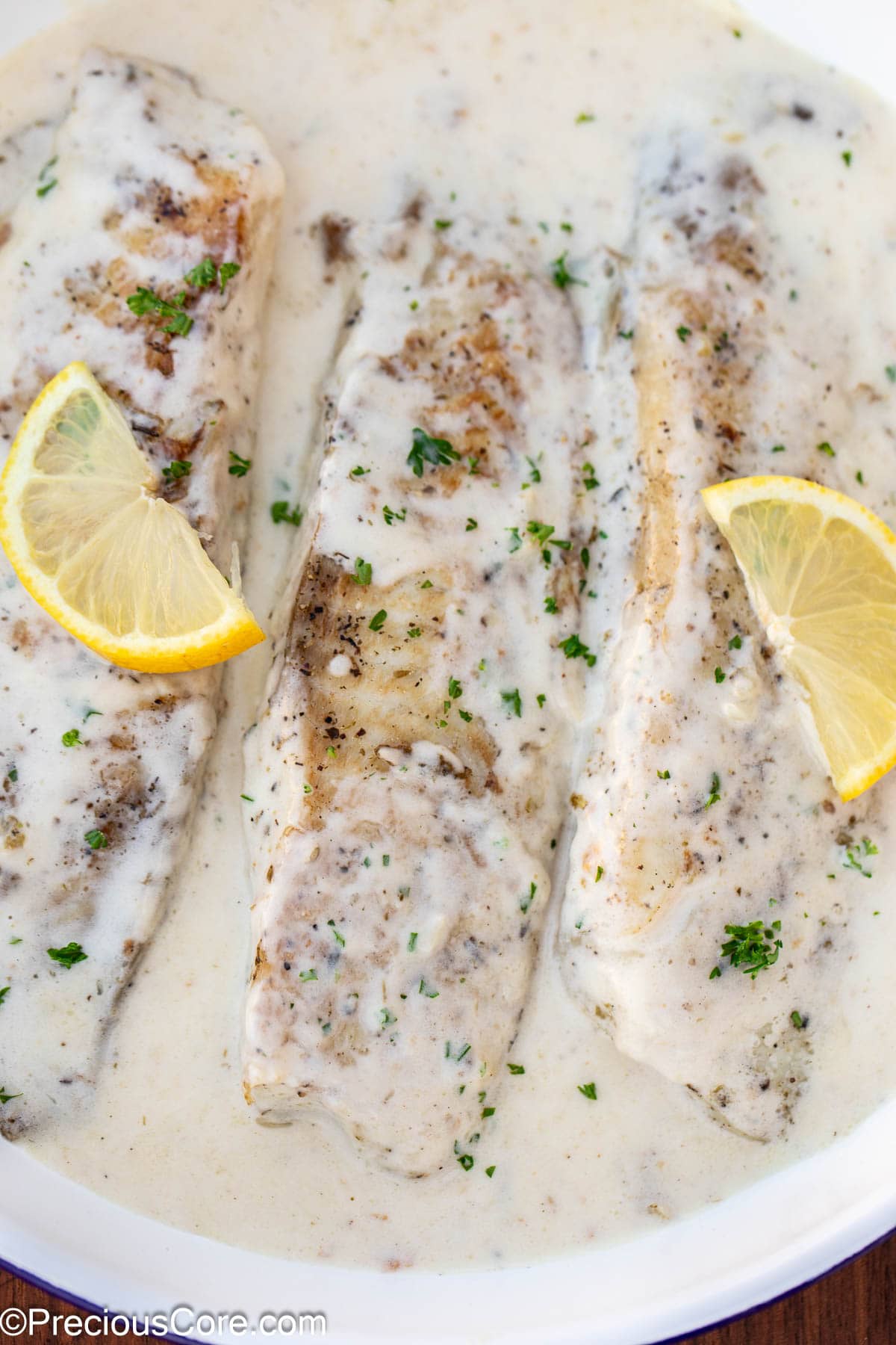Cooked fish fillets in a skillet with white sauce.