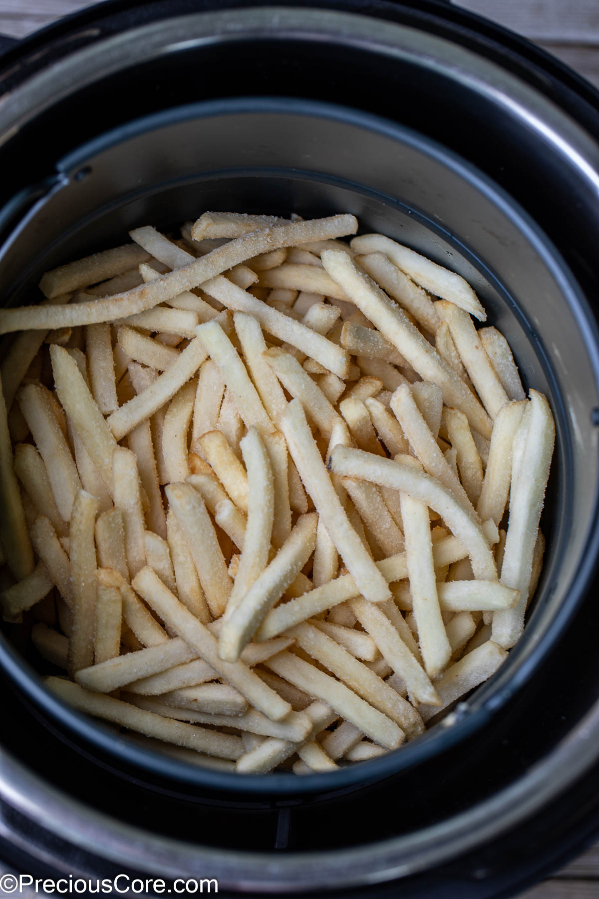 Frozen fries in a round air fryer basket.