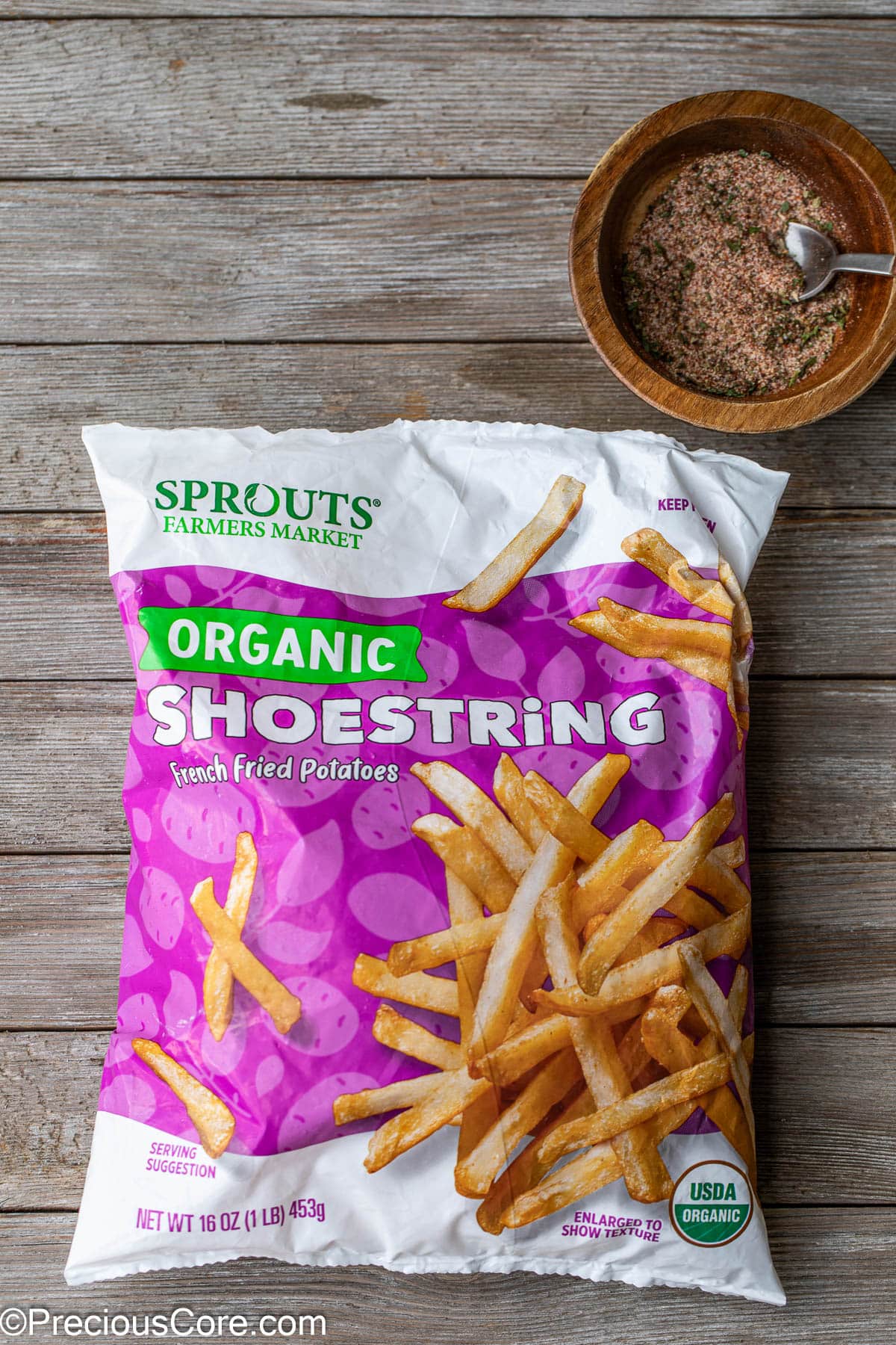 A bag of frozen potato fries and a bowl of friesseasoning nearby.